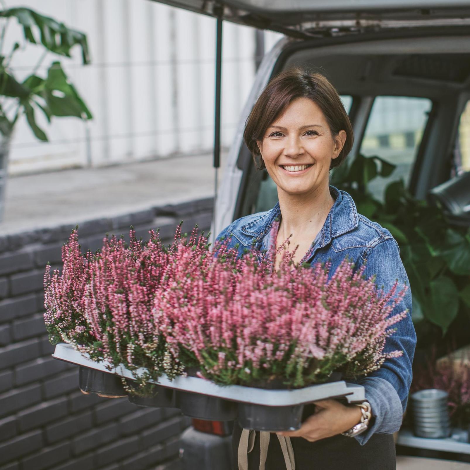 Smiling woman loading car trunk filled with different type of flowers.