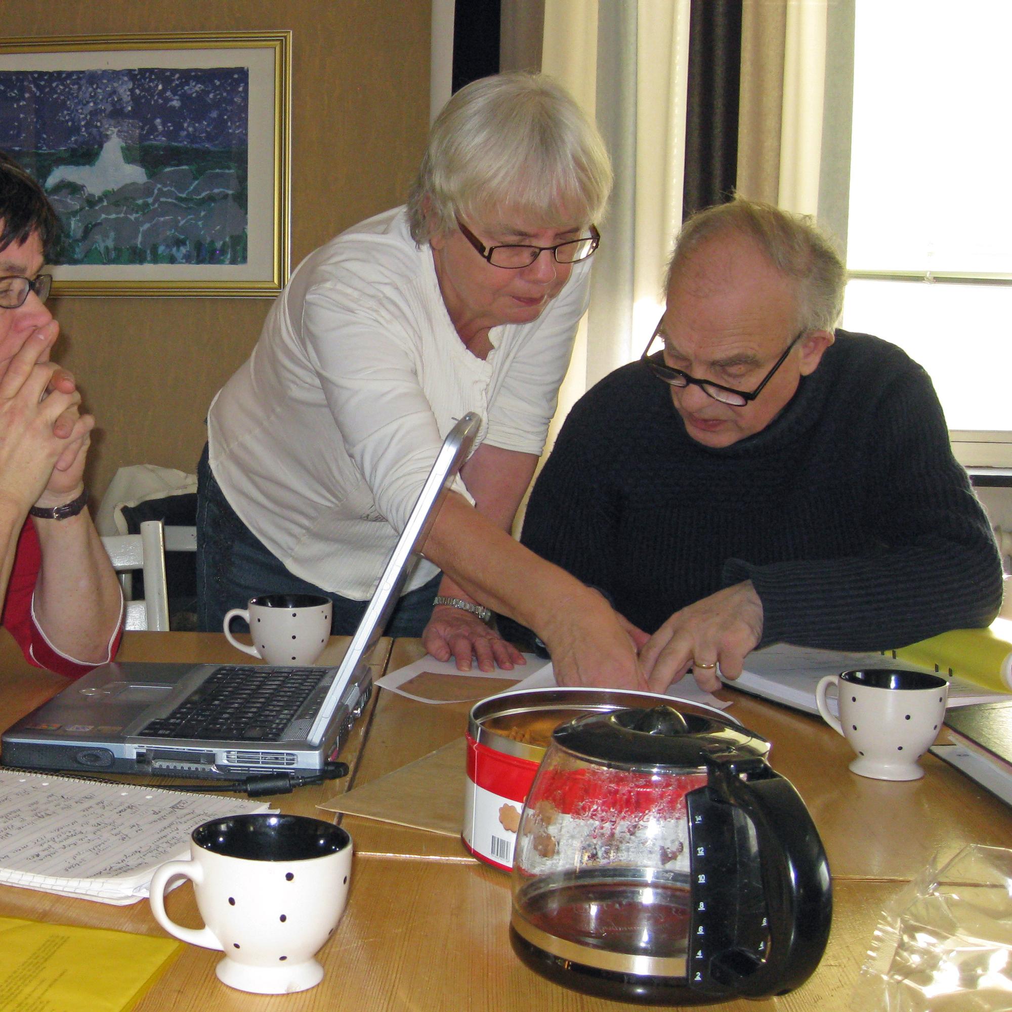Tre pensionärer sitter och arbetar vid ett köksbord