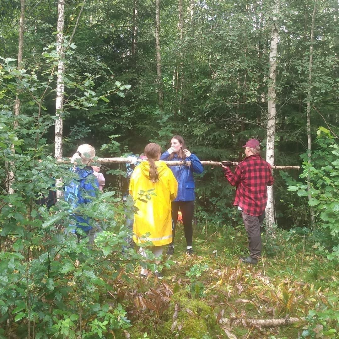 Fyra personer håller en stor pinne i skogen