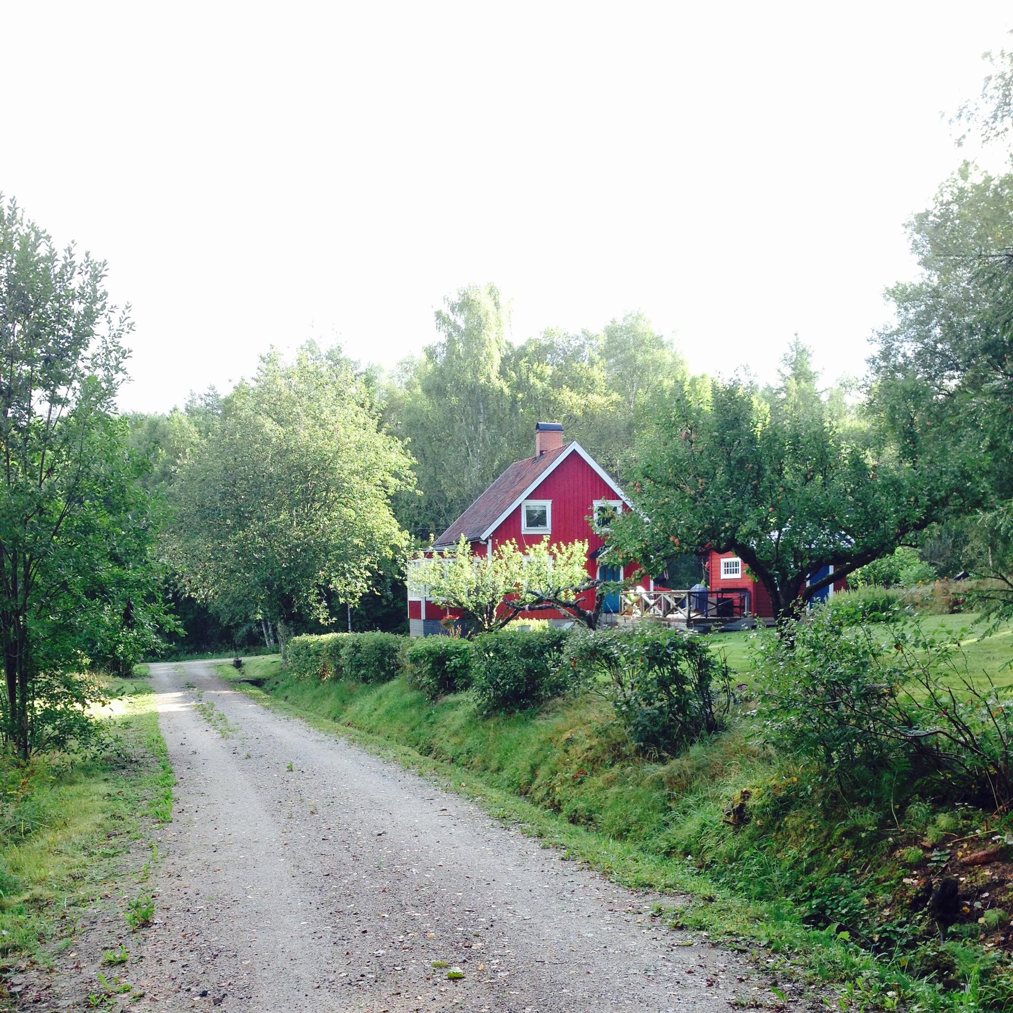 Ett rött hus vid slutet av en grusväg framför en skog