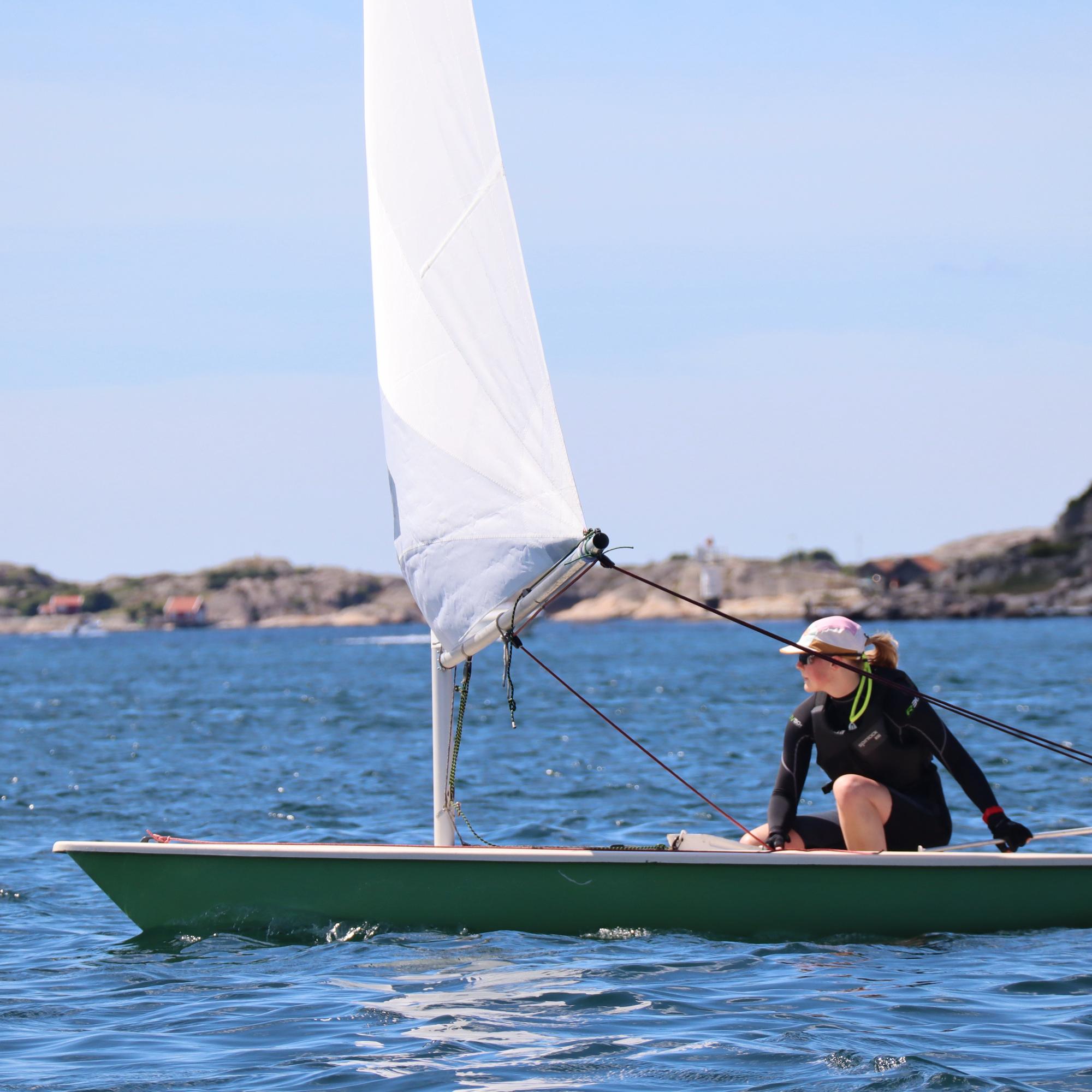 En tjej sitter och seglar i en segelbåt på havet