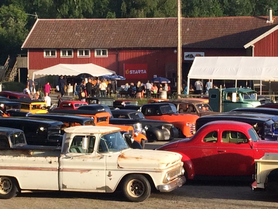Många gamla bilar parkerade på rad framför en folksamling i ett partytält