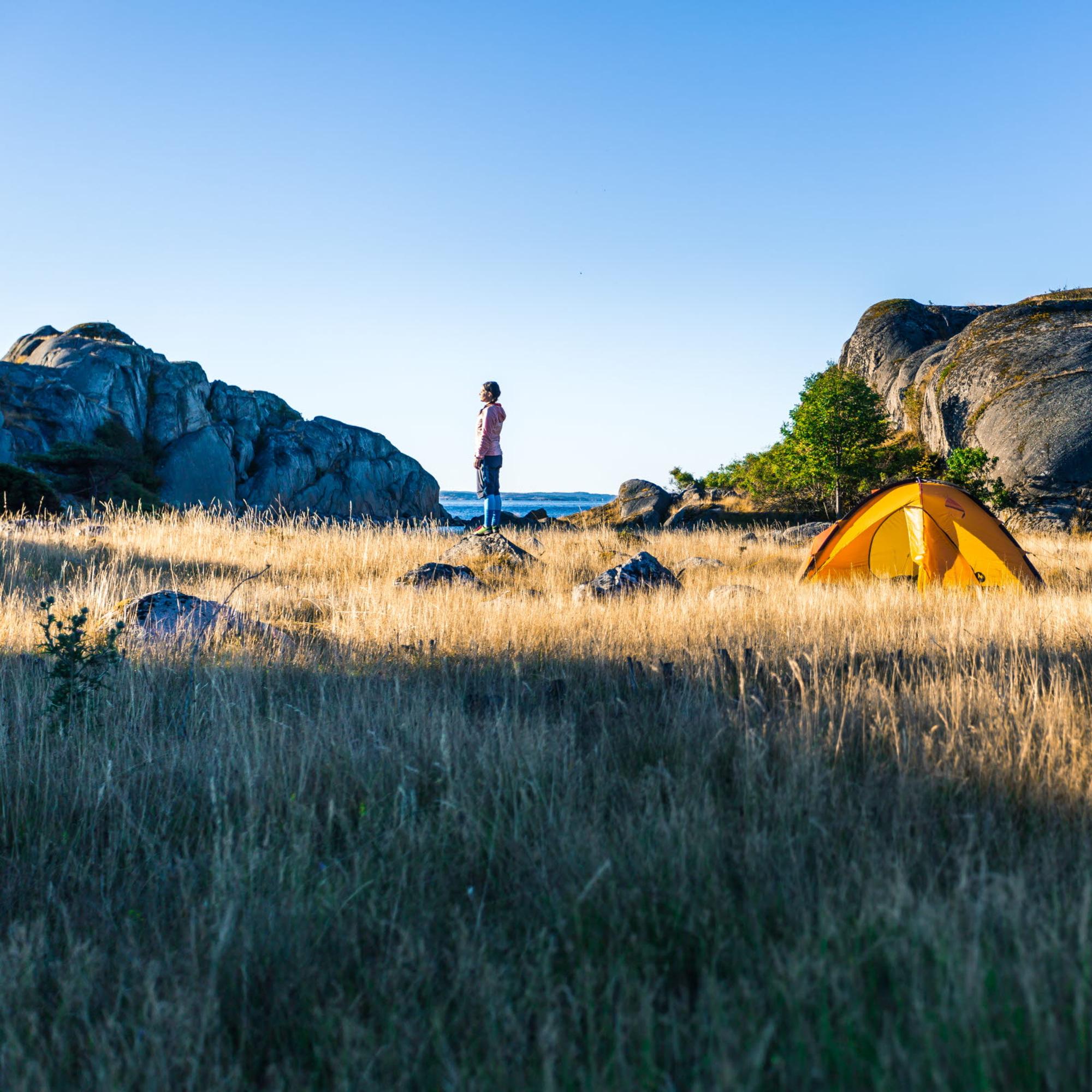 En person tältar på en åker vid havet