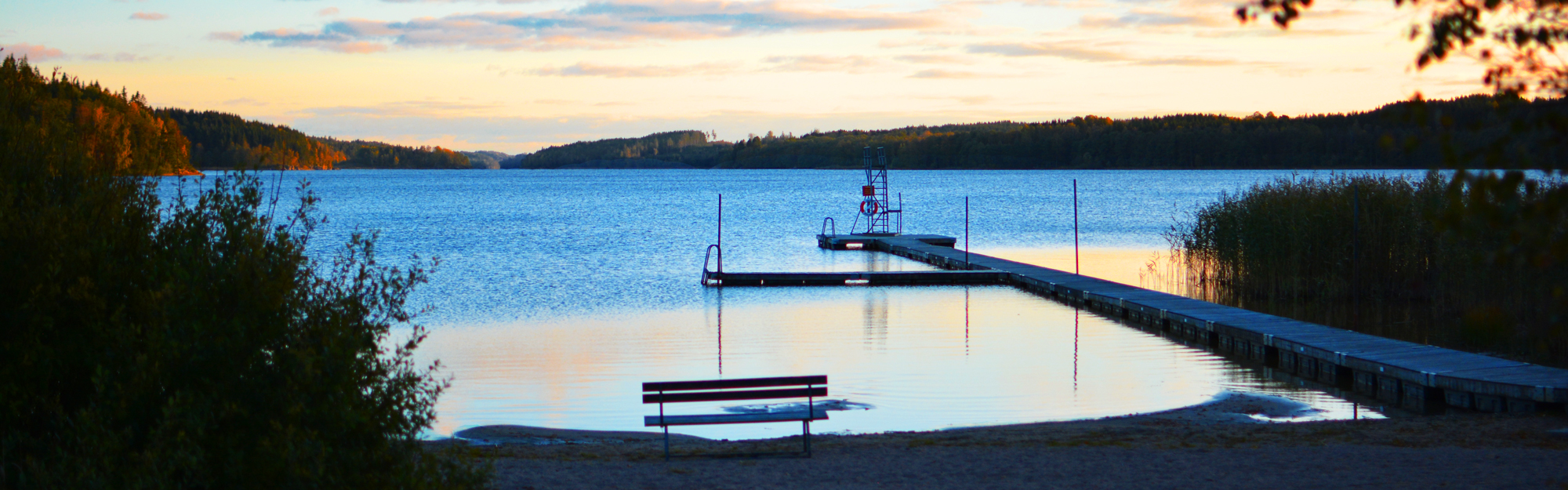 Solnedgång över sjö och badplats.