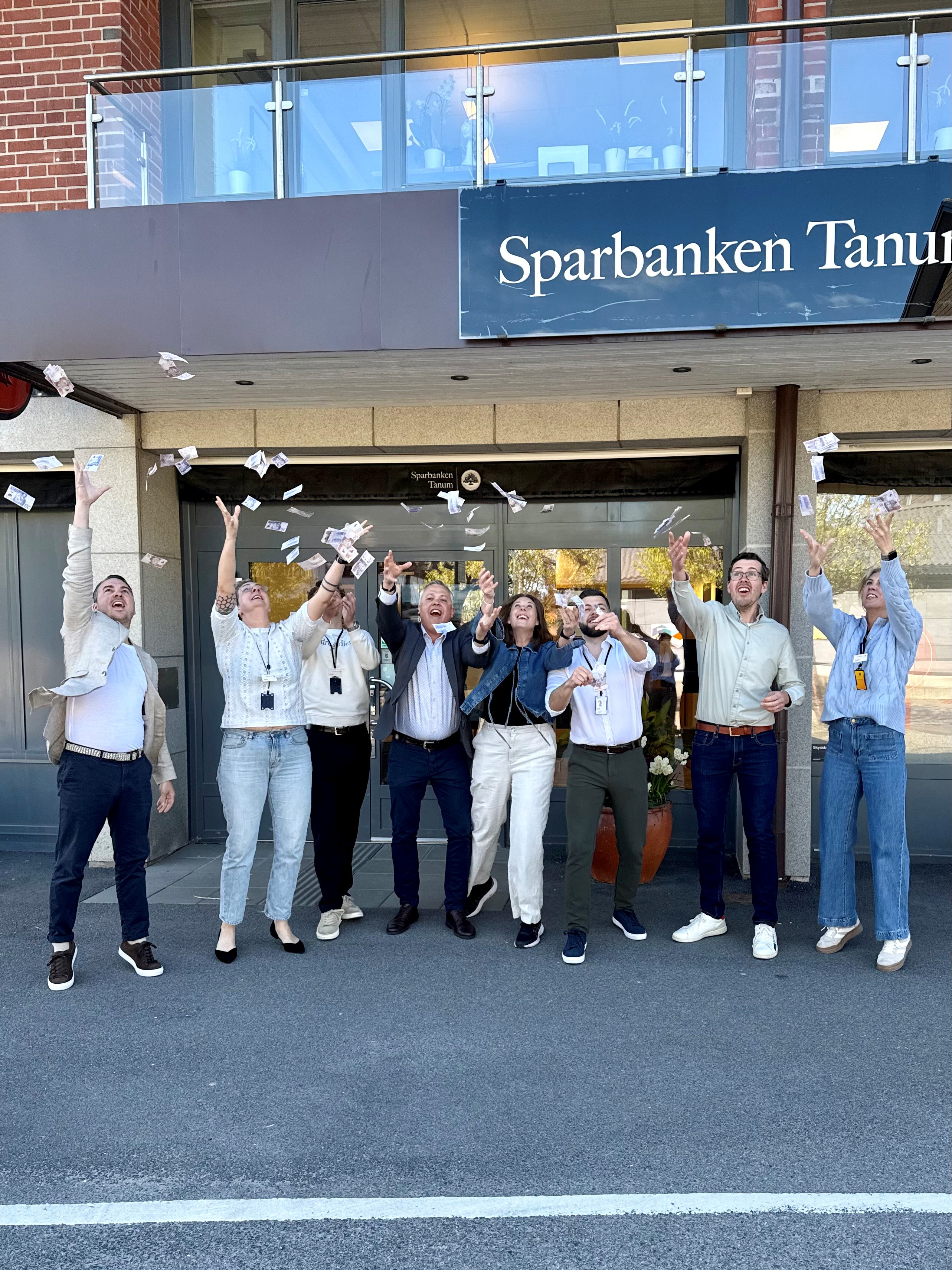 Gruppbild över några i personalen på Sparbanken Tanum som kastar pengar i luften